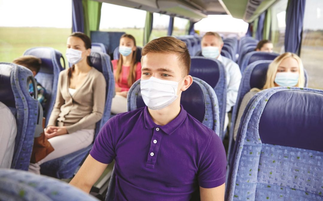 transport, tourism, road trip and people concept - young man wearing face protective medical mask for protection from virus disease sitting in travel bus or train